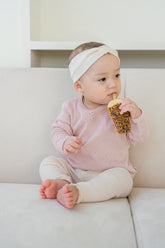 Baby sitting on a couch wearing the Avauma Peach Glow Set in Pale Peach – made from soft materials with a neat button detail for comfortable wear